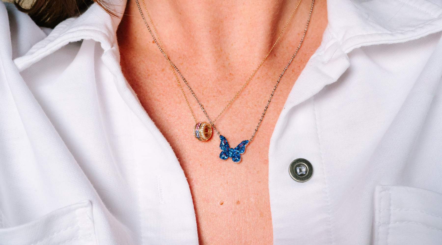 Layered 14K gold necklaces with blue butterfly and gemstone pendant, worn with white shirt