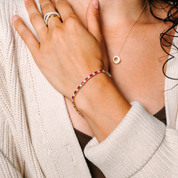 Woman wearing 14K gold ruby and diamond bracelet, rings, and pendant necklace with cozy sweater