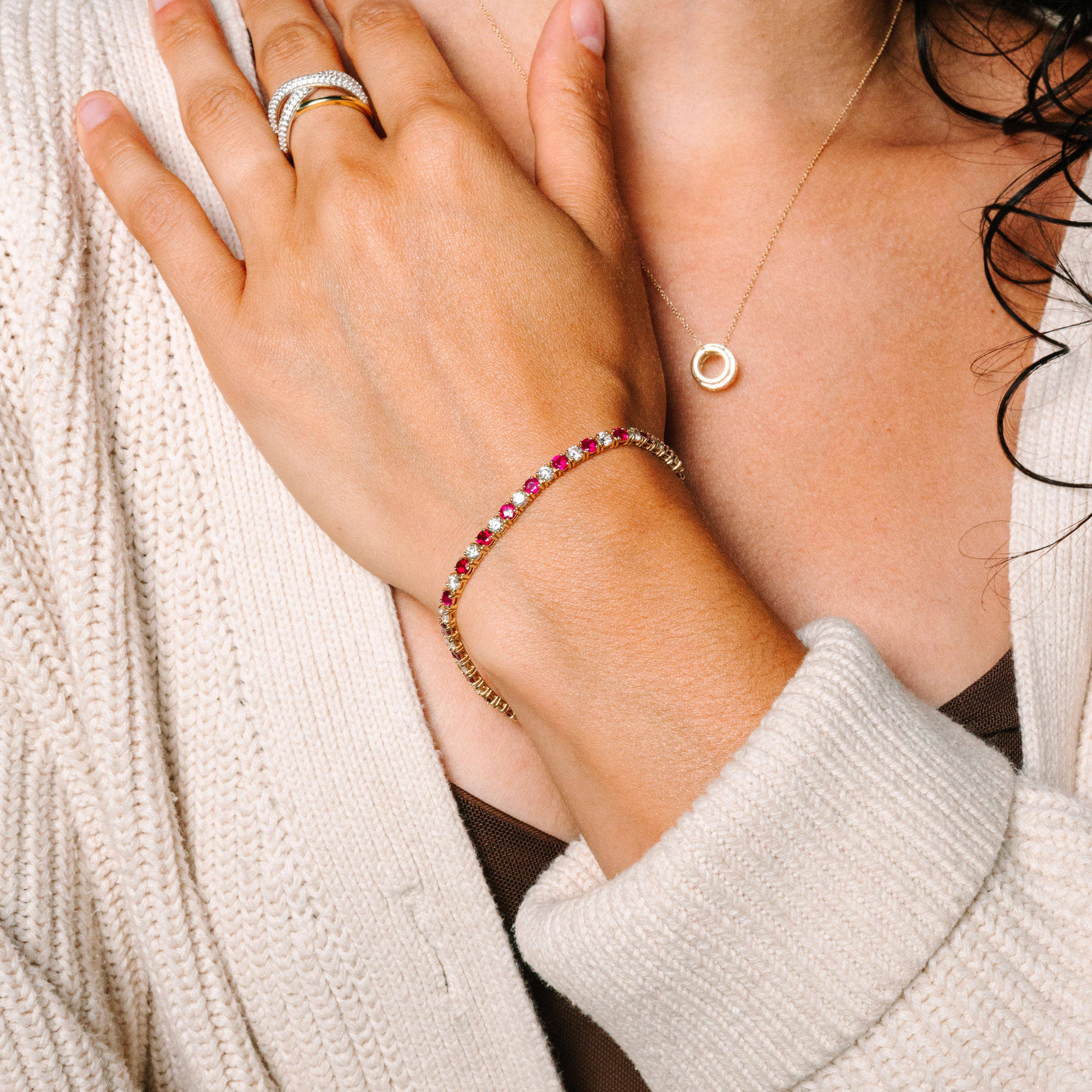 Woman wearing 14K gold ruby and diamond bracelet, stackable rings, and minimalist necklace