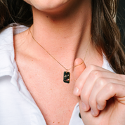 14K gold necklace with black enamel pendant, diamond accents, and ruby detail, worn by woman in white shirt