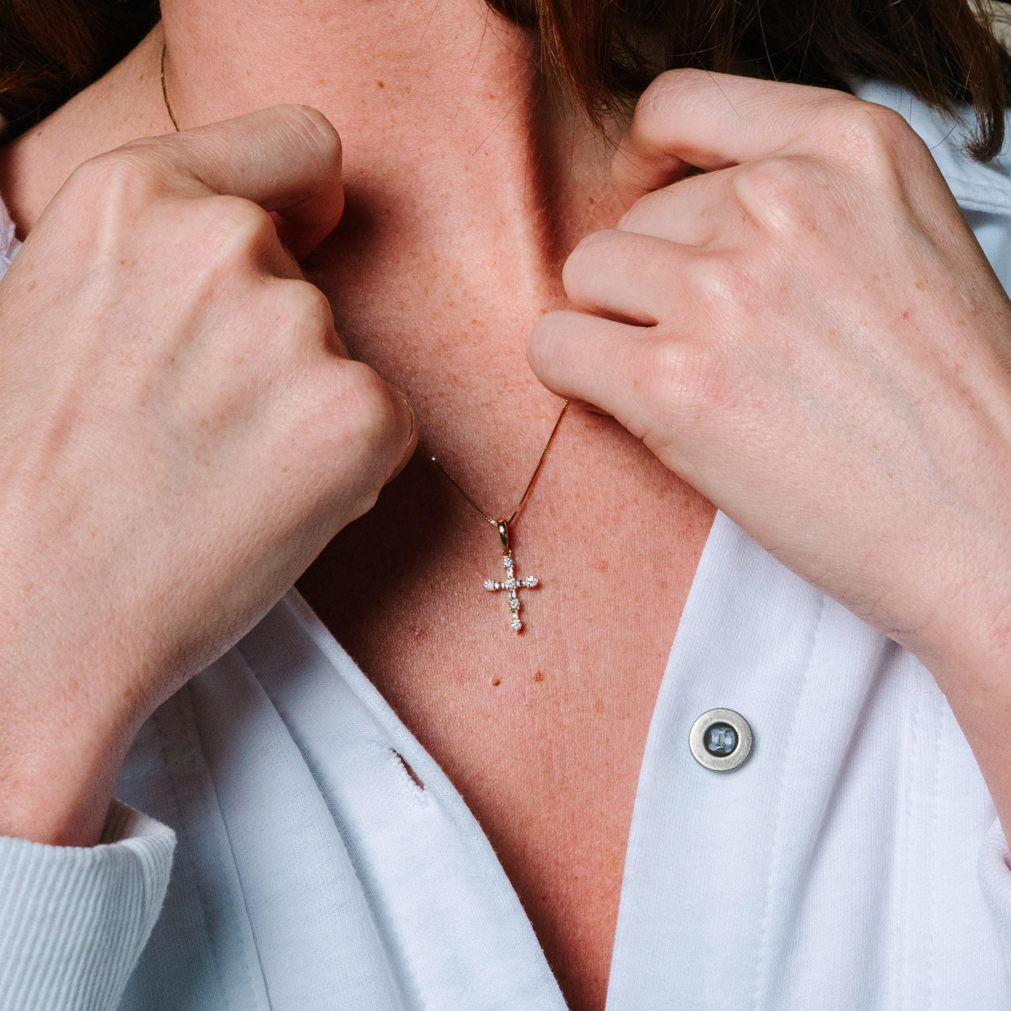 Woman wearing 14K gold diamond cross necklace, adjusting delicate pendant on collarbone