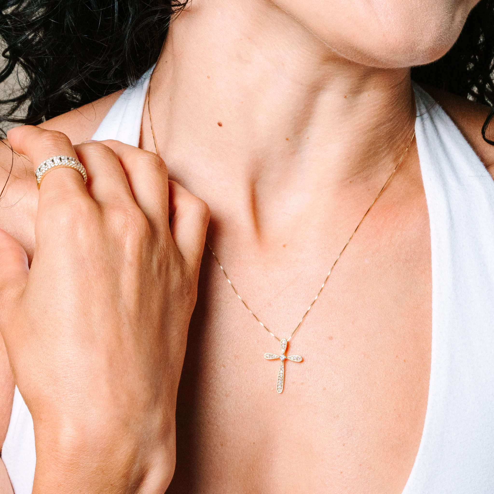 14K gold cross necklace with diamonds, paired with diamond band ring, worn by woman in white top