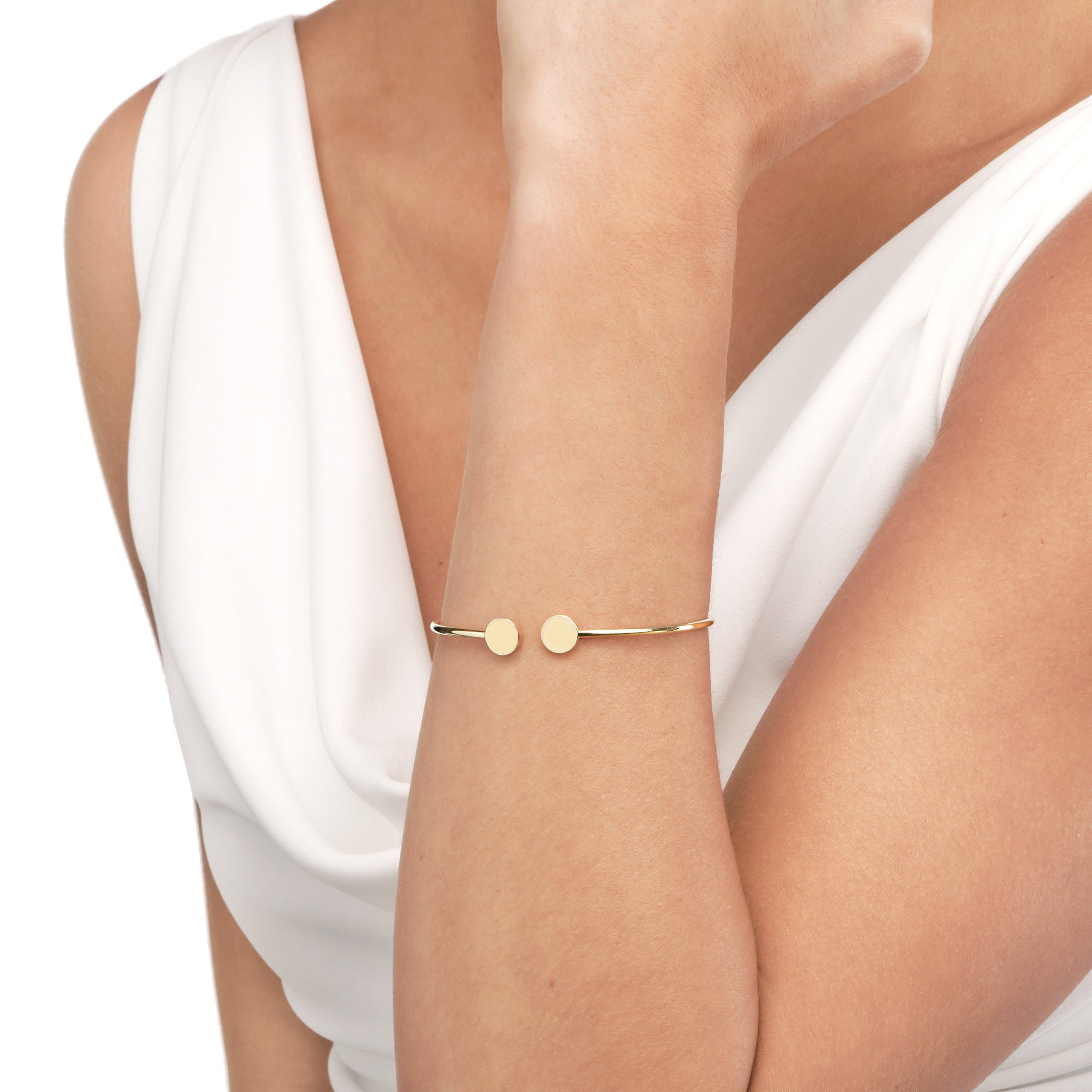 Delicate 14K gold bracelet with two round discs, worn on wrist with white draped top