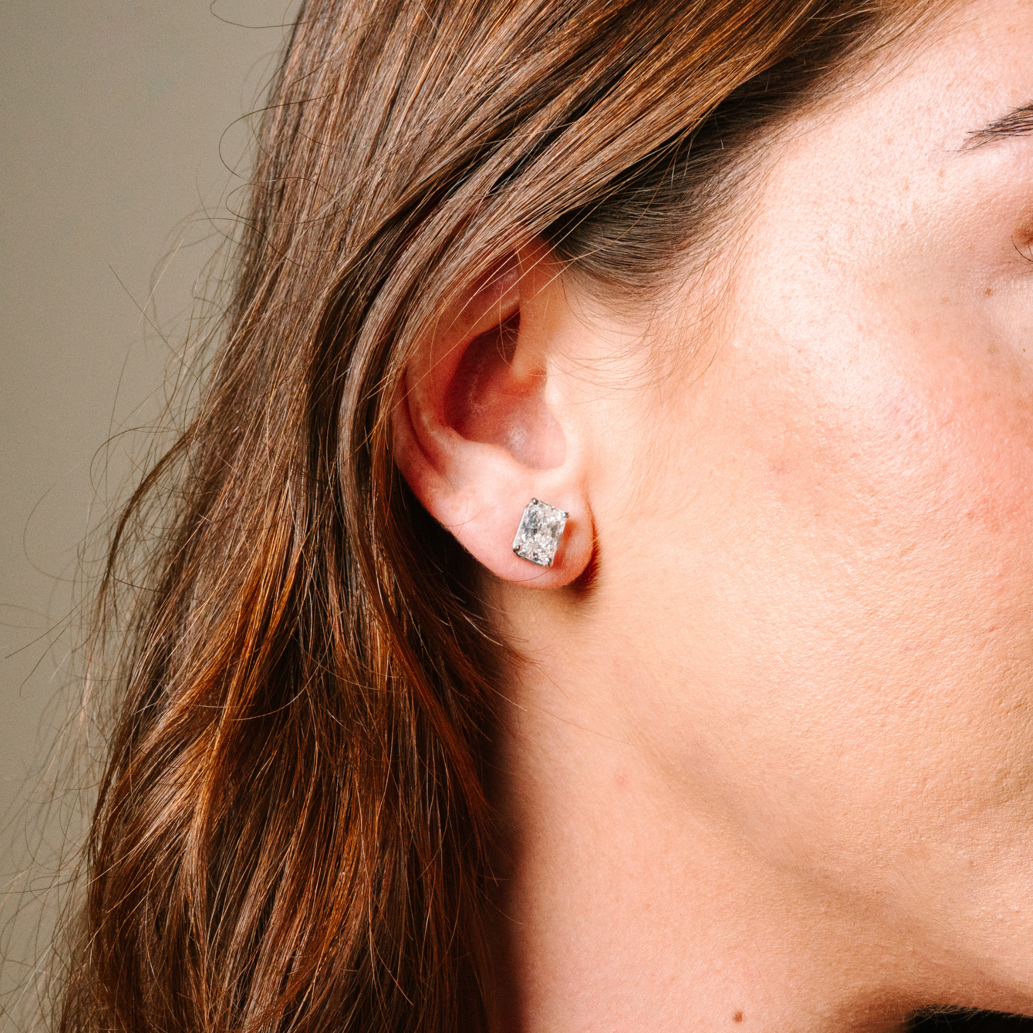 Radiant cut diamond stud earring in 14K gold, worn on ear with brown hair