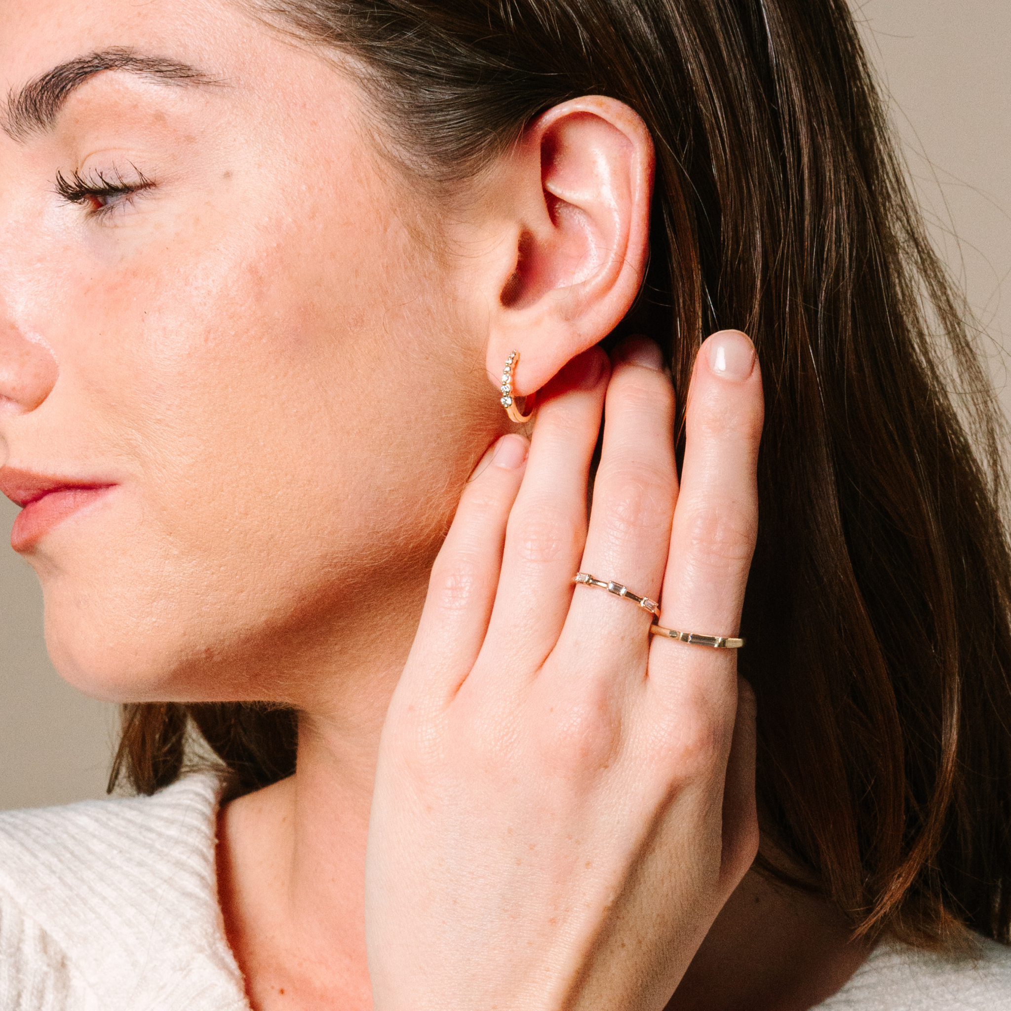 Woman wearing 14K gold diamond hoop earrings and delicate rings, showcasing timeless fine jewelry.