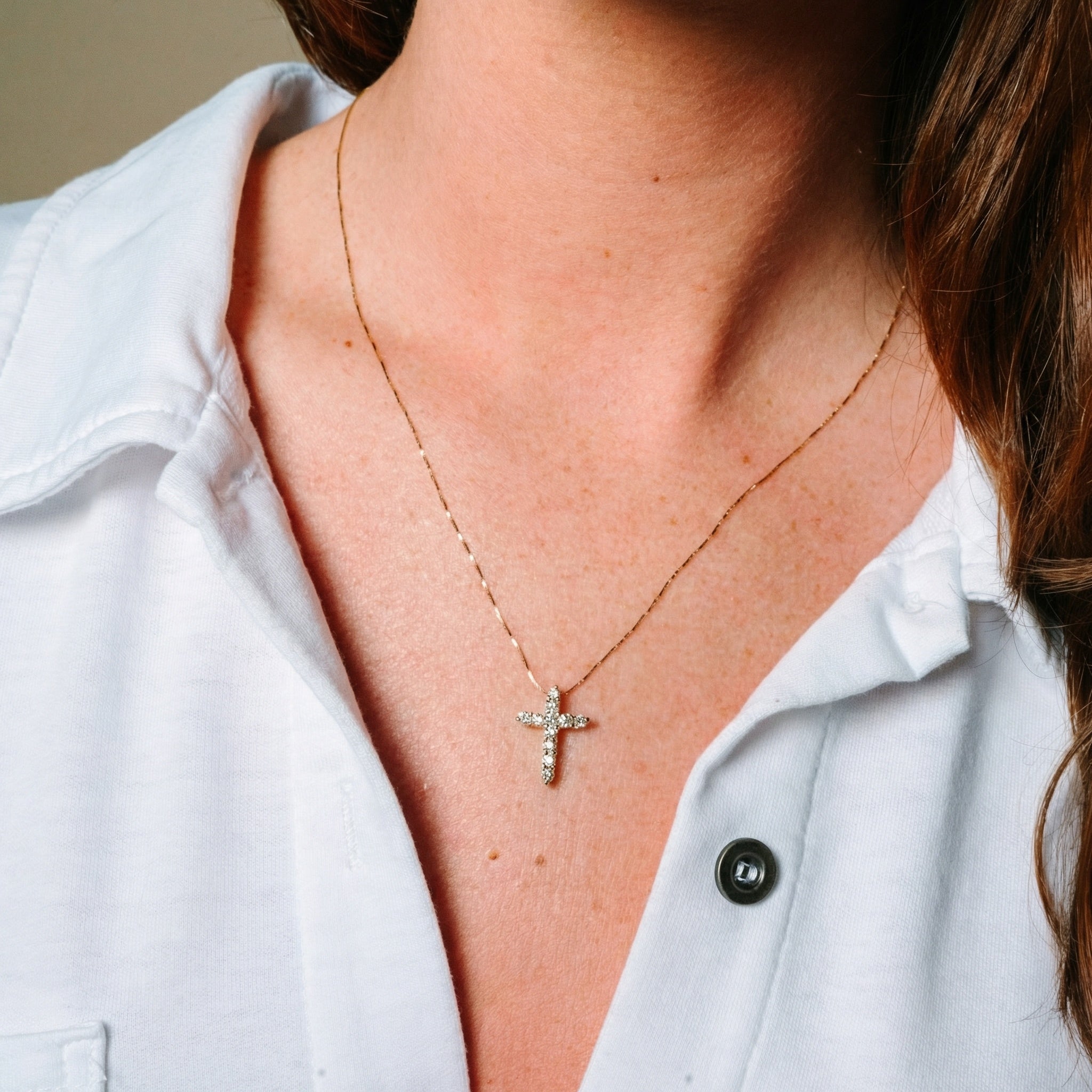 Delicate 14K gold cross necklace with diamond accents, worn with a white shirt for everyday elegance.