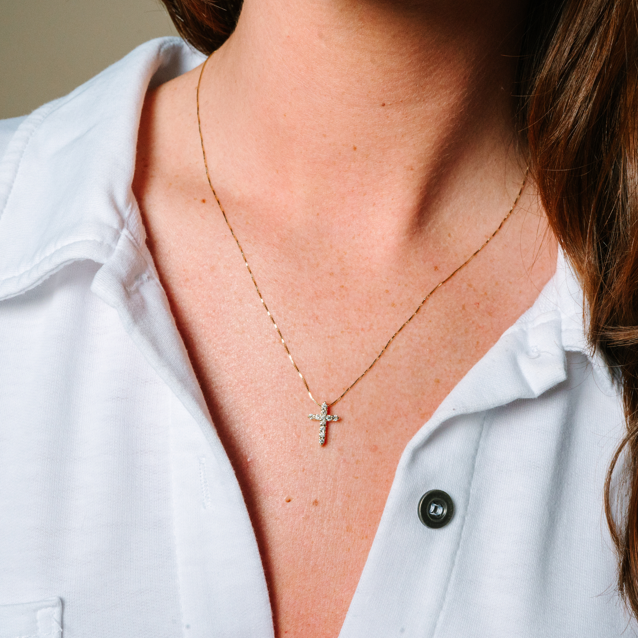 Delicate 14K gold cross necklace with diamond accents, worn with a white shirt for everyday elegance.