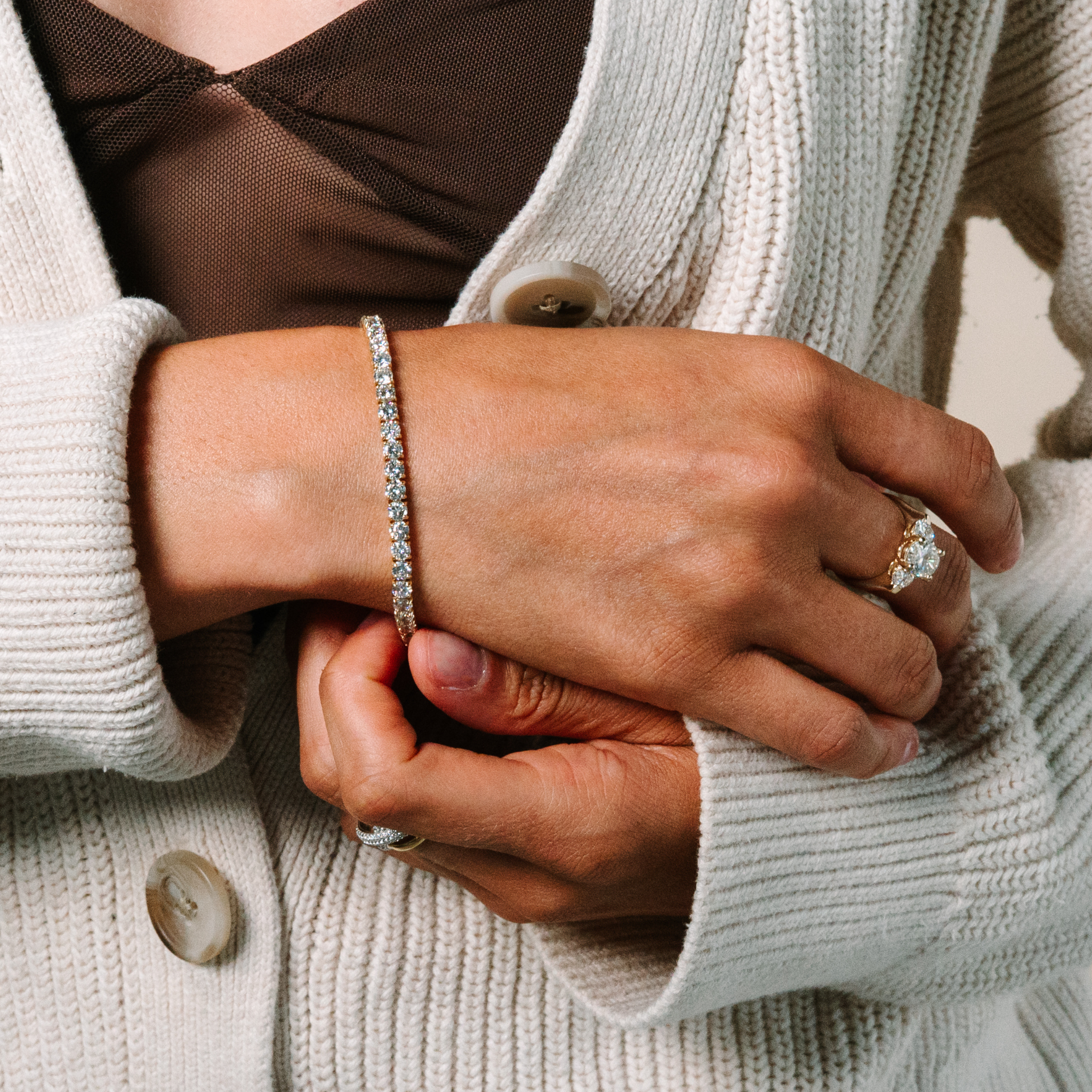 Woman wearing 14K gold diamond tennis bracelet and diamond ring, styled with cozy knit cardigan for everyday elegance.