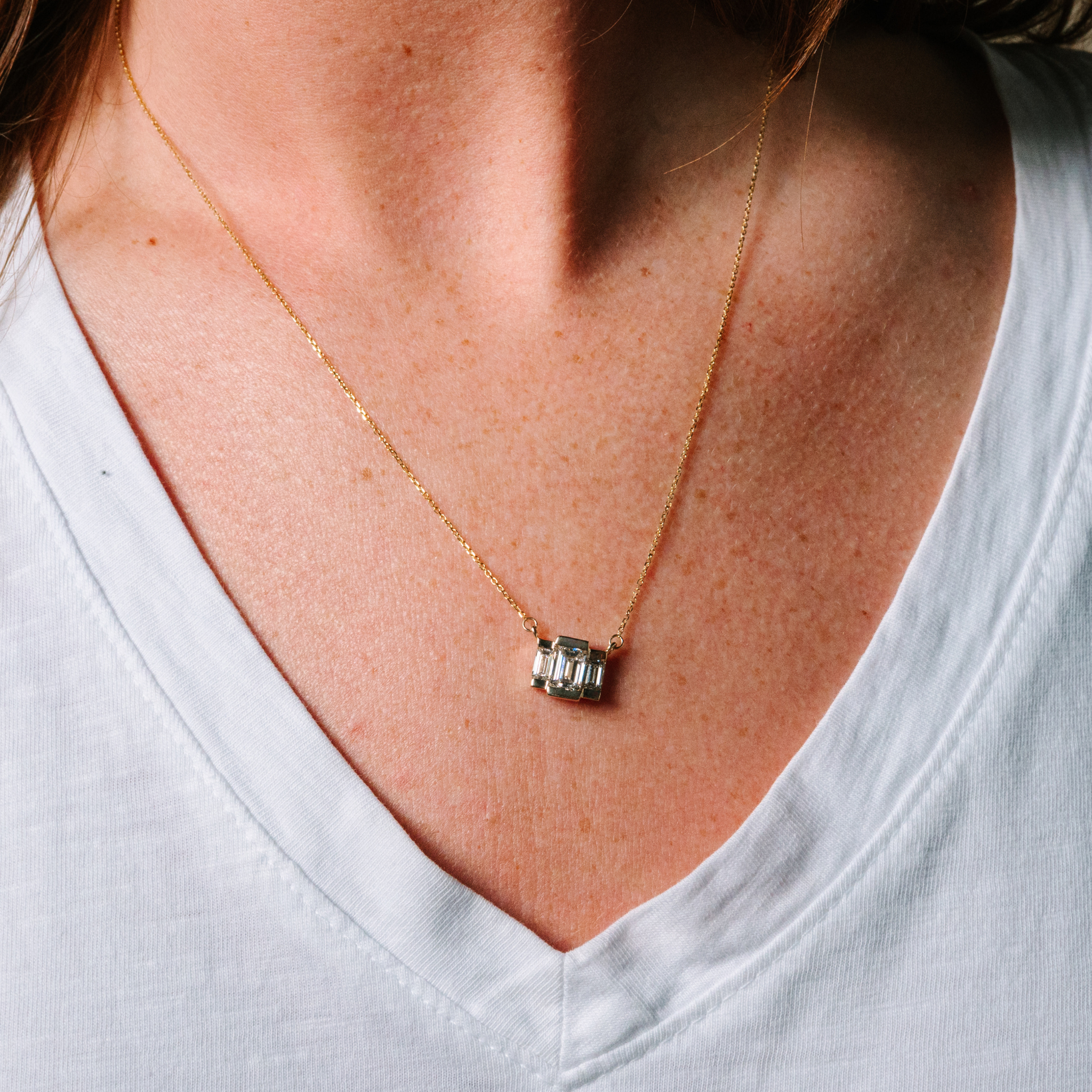 14K gold necklace with baguette diamond pendant, worn close to neck on white V-neck top