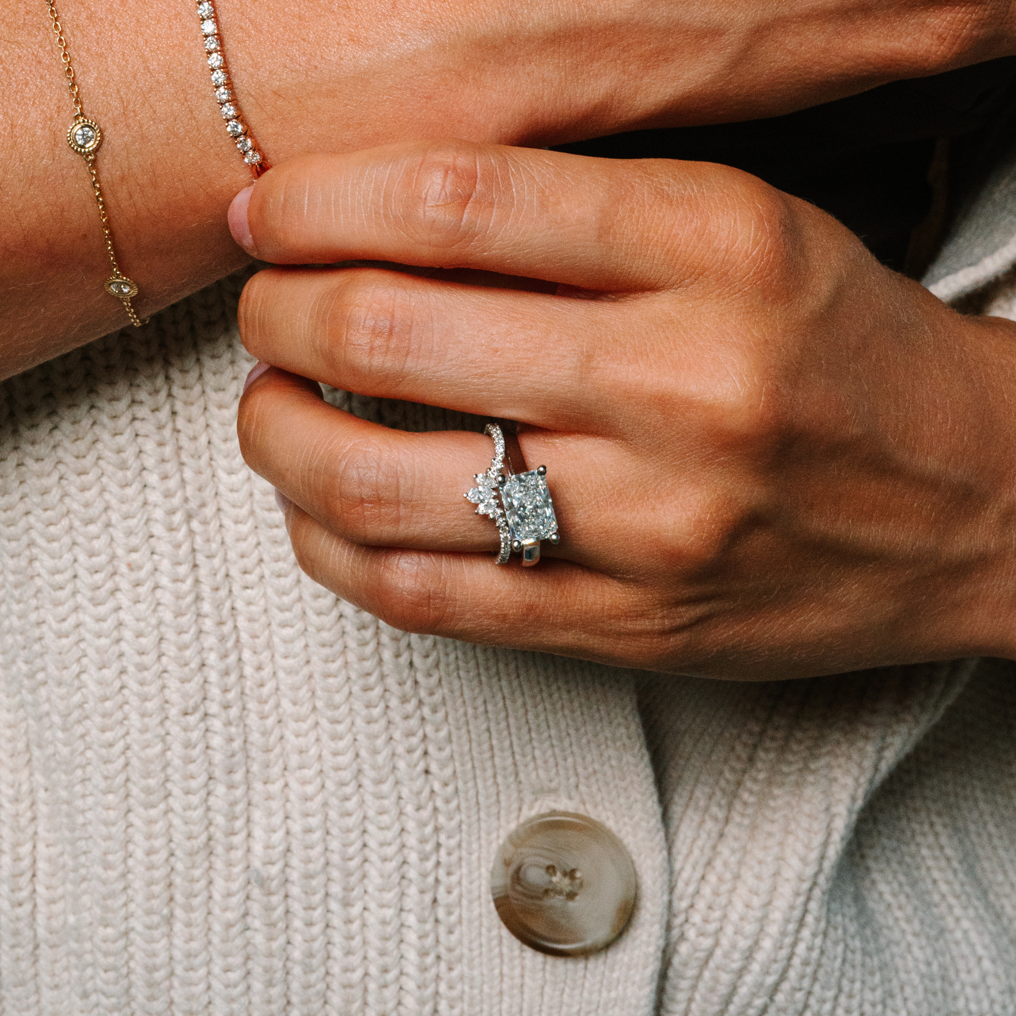 Elegant diamond engagement ring with side accents, paired with gold bracelet and diamond tennis bracelet on hand