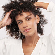 Woman wearing 14K gold hoop earrings, curly hair, white blouse, timeless fine jewelry