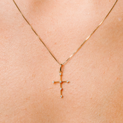 Delicate 14K gold cross necklace with diamond accents, worn on skin for everyday elegance.