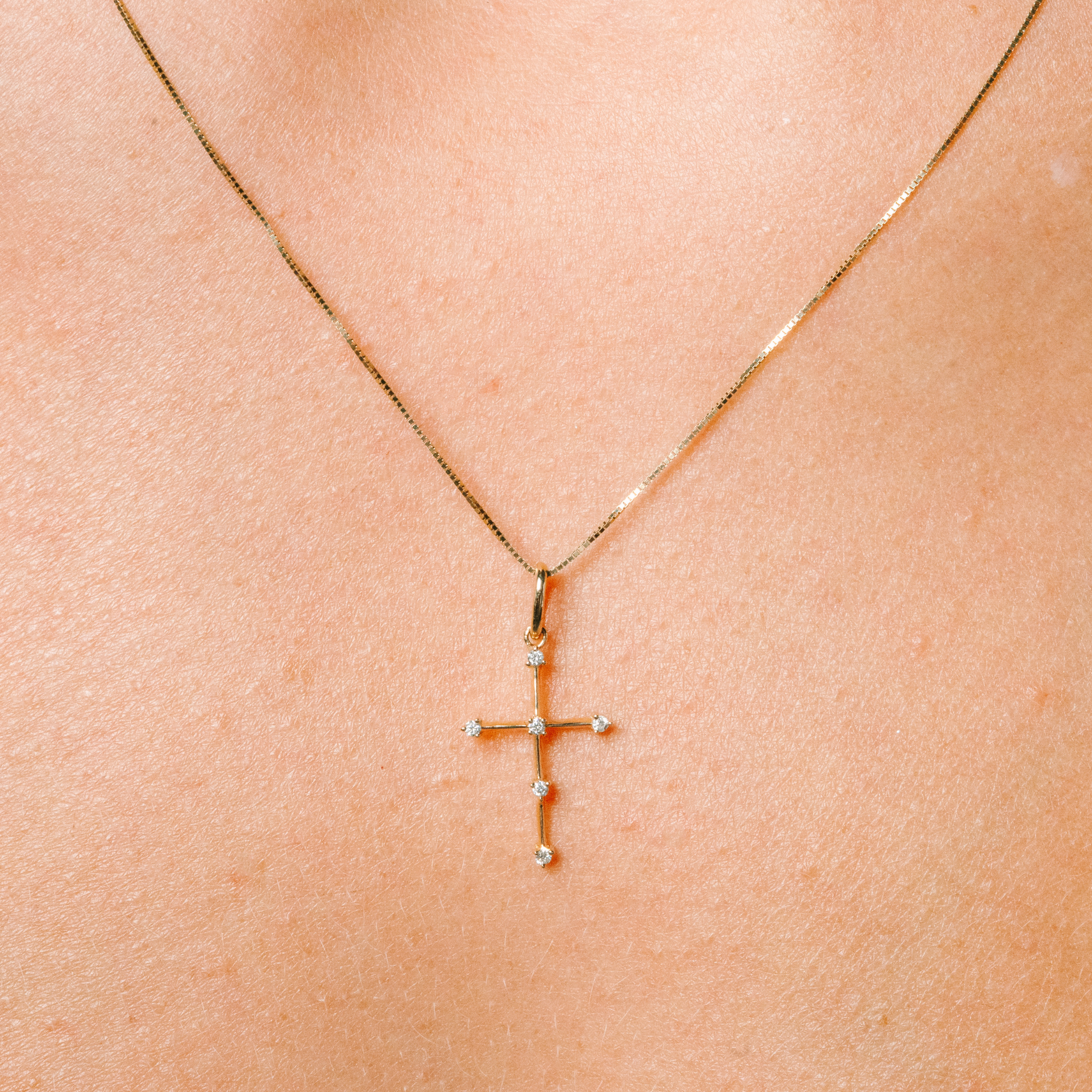 Delicate 14K gold cross necklace with diamond accents, worn on skin for everyday elegance.