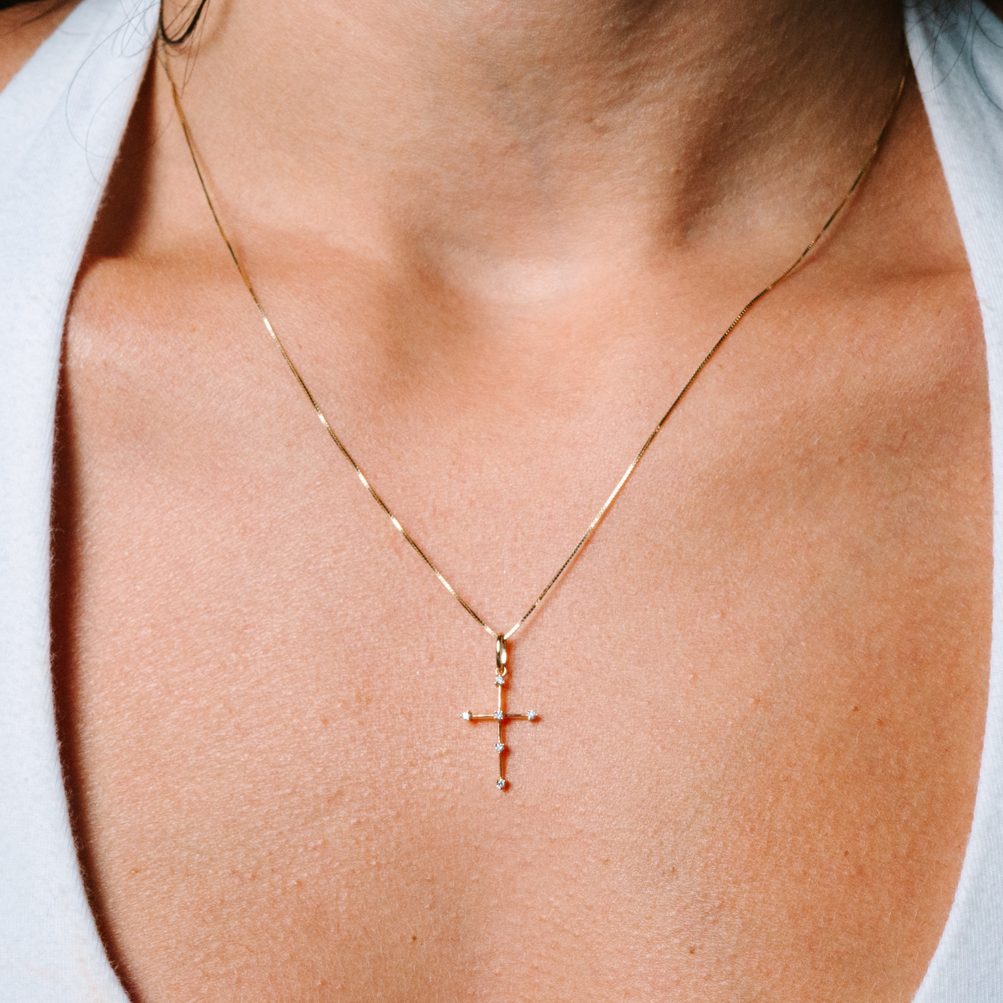 Delicate 14K gold cross necklace with diamond accents, worn close to the collarbone for everyday elegance.