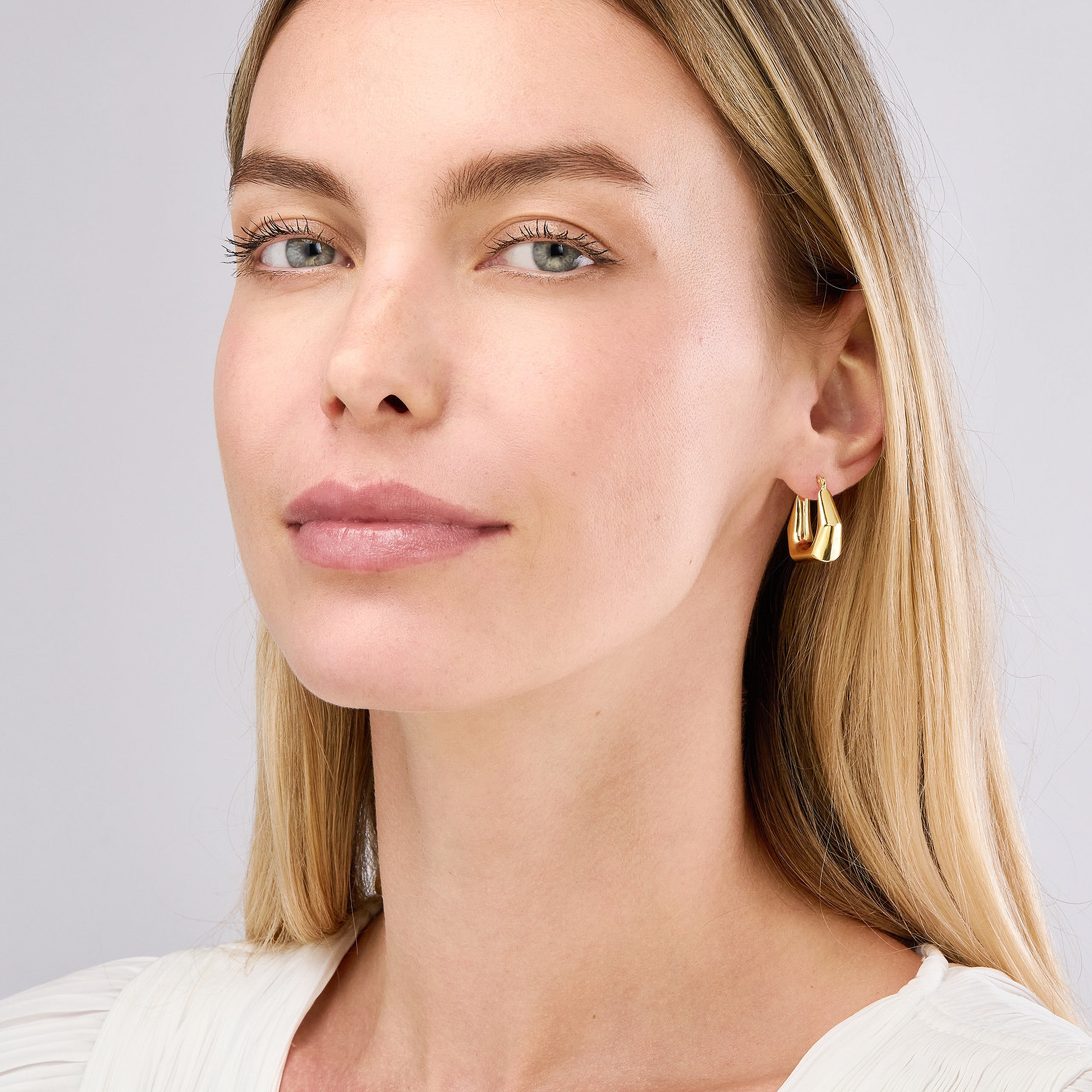 Woman wearing 14K gold geometric hoop earrings, timeless fine jewelry for everyday wear