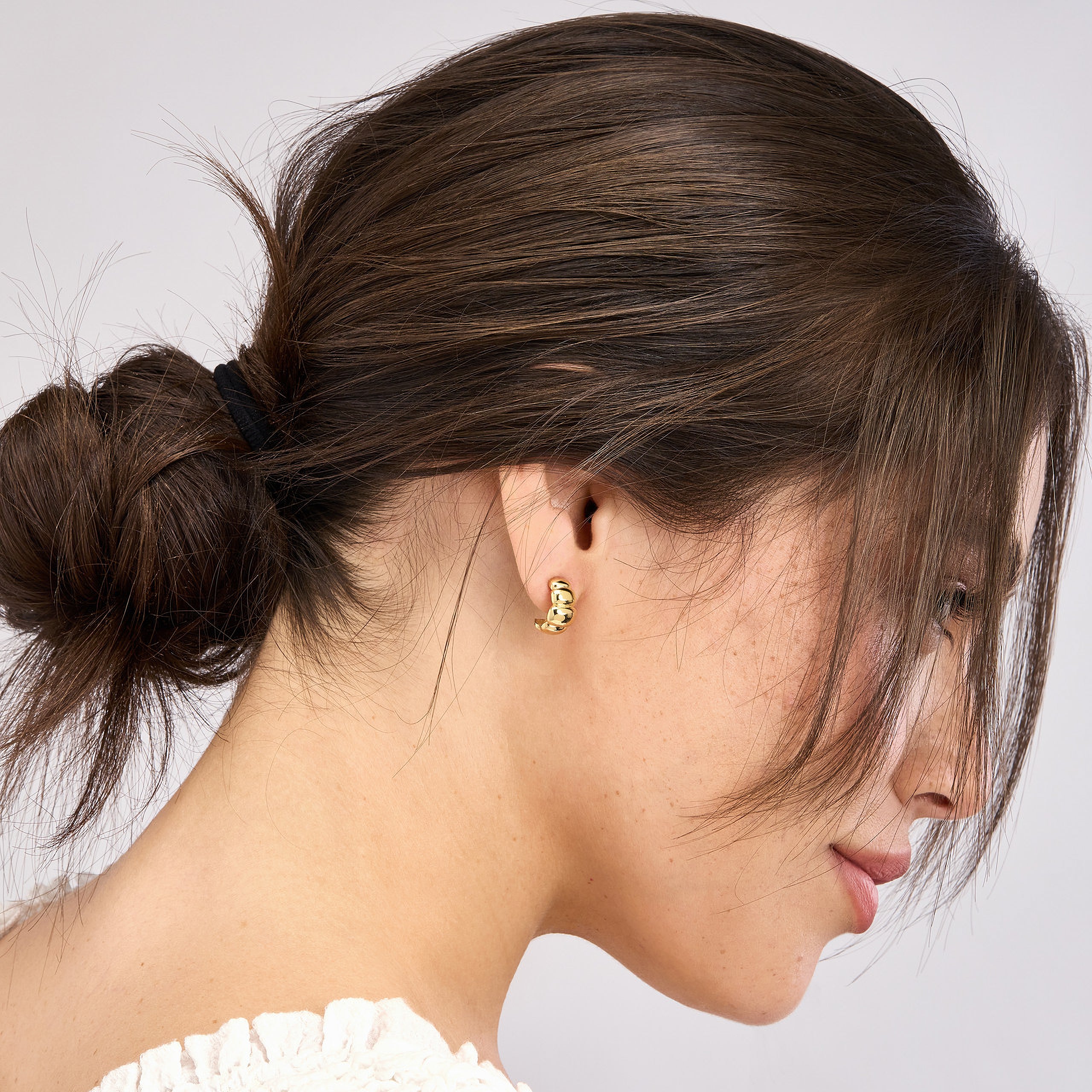 Gold hoop earring with textured design, worn by woman with low bun, showcasing everyday fine jewelry style