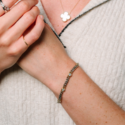 Woman wearing 14K gold diamond chain bracelet, clover pendant necklace, and stackable rings on hand