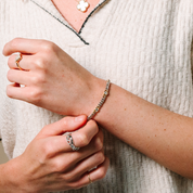 Woman adjusting 14K gold diamond chain bracelet with matching rings and clover pendant necklace