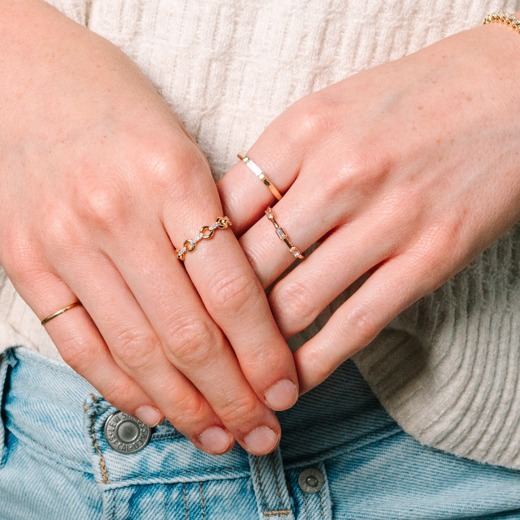 Delicate 14K gold rings with diamonds, styled on hands over denim—everyday fine jewelry for layering.