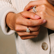 Elegant diamond rings in 14K gold, featuring a floral cluster design and intertwined bands, worn on hands in a cozy sweater.