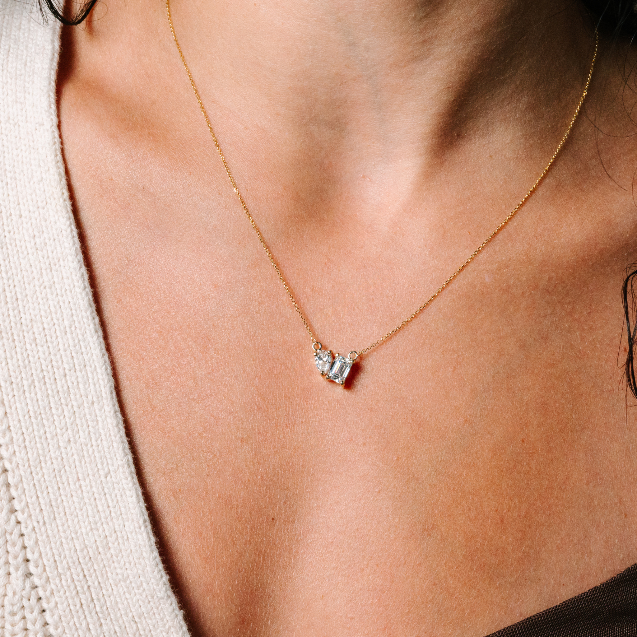 14K gold necklace with two diamond pendants, one heart and one emerald cut, worn on model