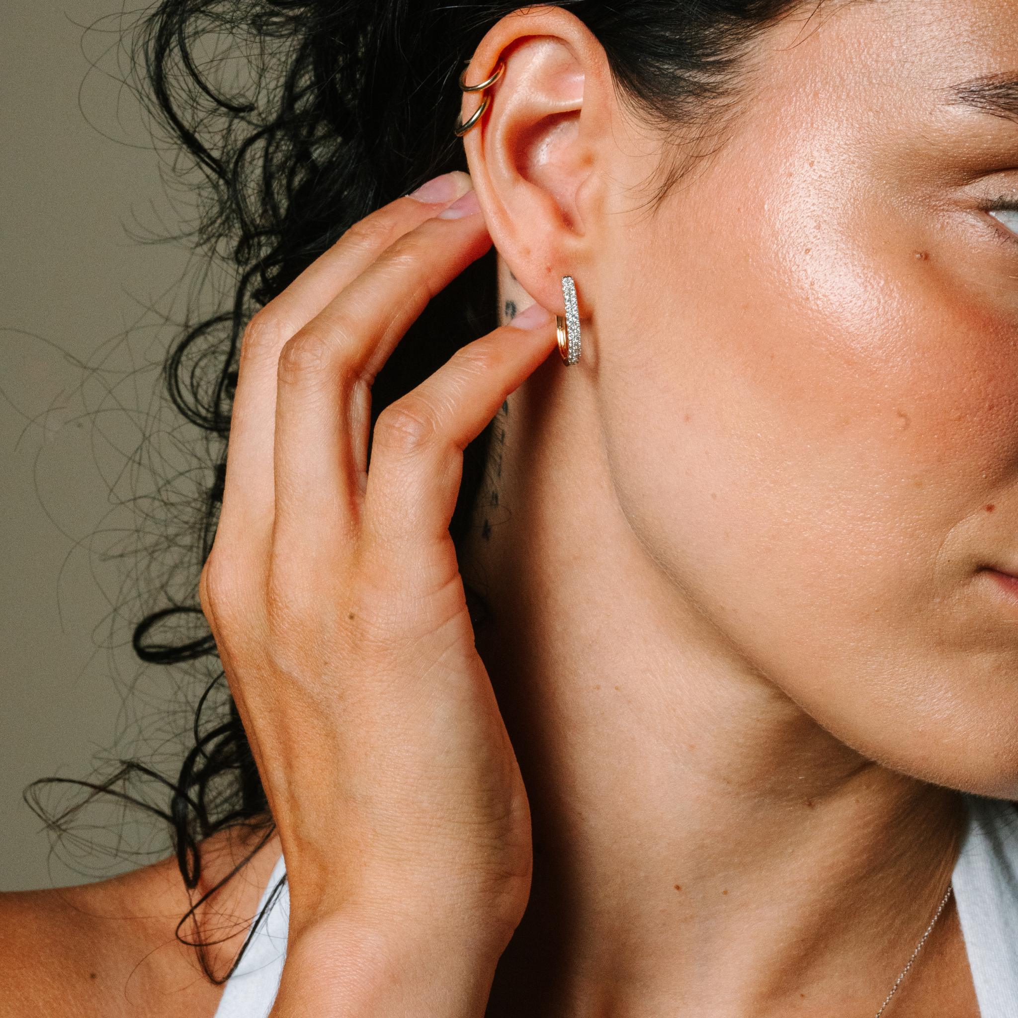 Woman wearing 14K gold diamond hoop earrings, layered with delicate ear cuffs, showcasing timeless fine jewelry.